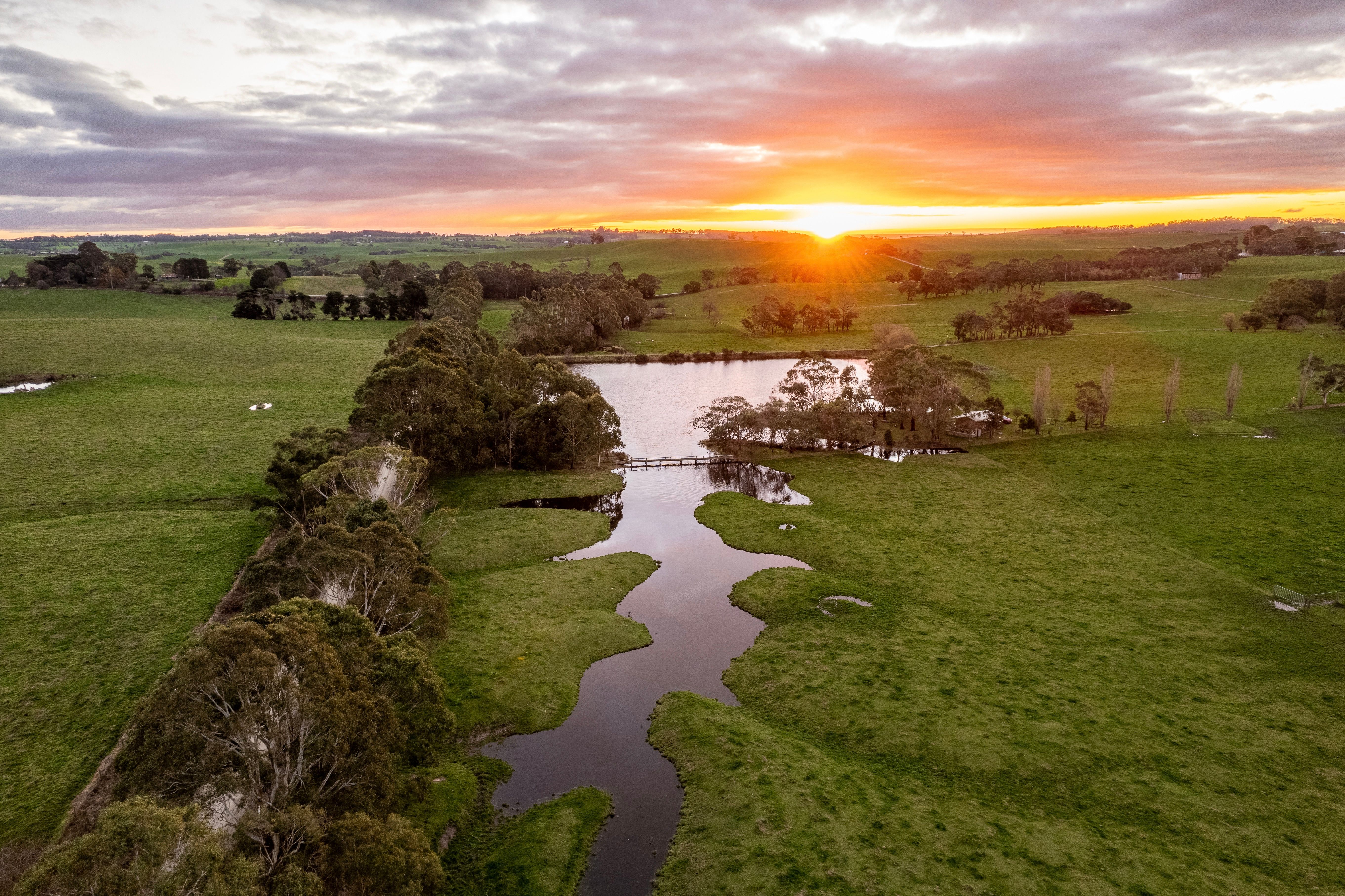 A creek winding through green pasture and tree lines at sunset